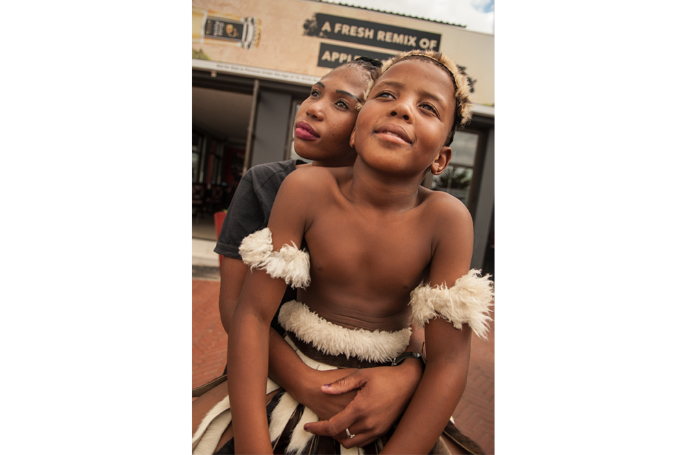 Soweto. Una mujer abraza a su hijo en Vilakazi. El chaval vestido de zulú interpreta bailes indígenas frente a los restaurantes en busca de propinas